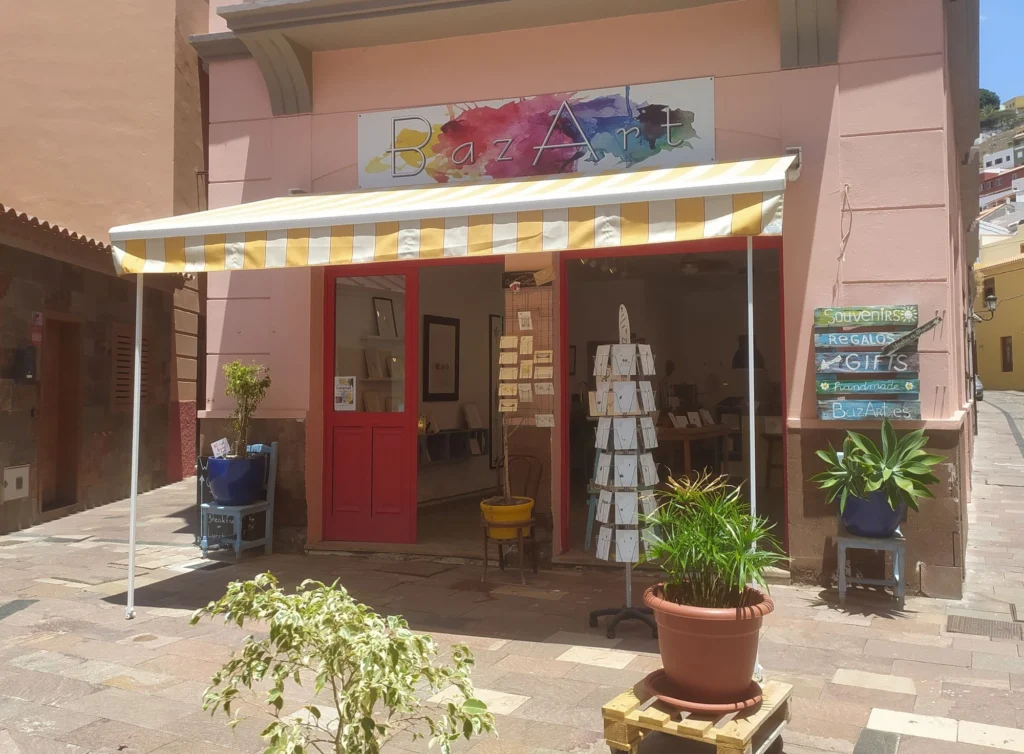 The BazArt shop in San Sebastián de La Gomera: pink façade, colourful BazArt sign, yellow-striped awning, red doors and a rack of hand-drawn cards